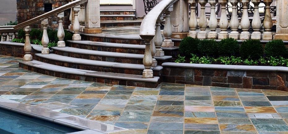Stone patio with steps, balustrade, and pool. Blue, brown, and gray stone. Green shrubbery.