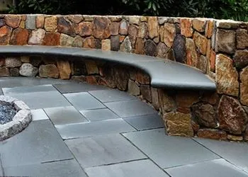 Curved stone bench along a rock wall beside a gray paved patio