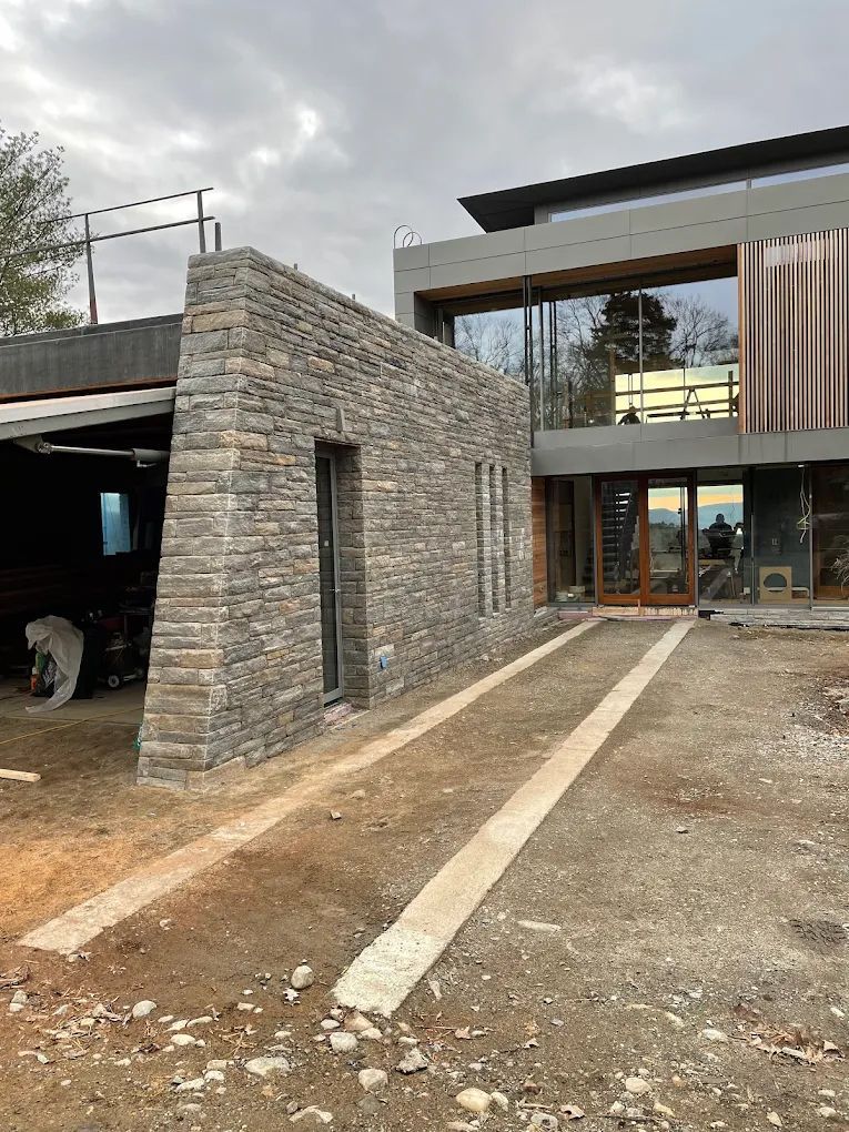 Modern house with a stone wall, driveway under construction, and cloudy sky.