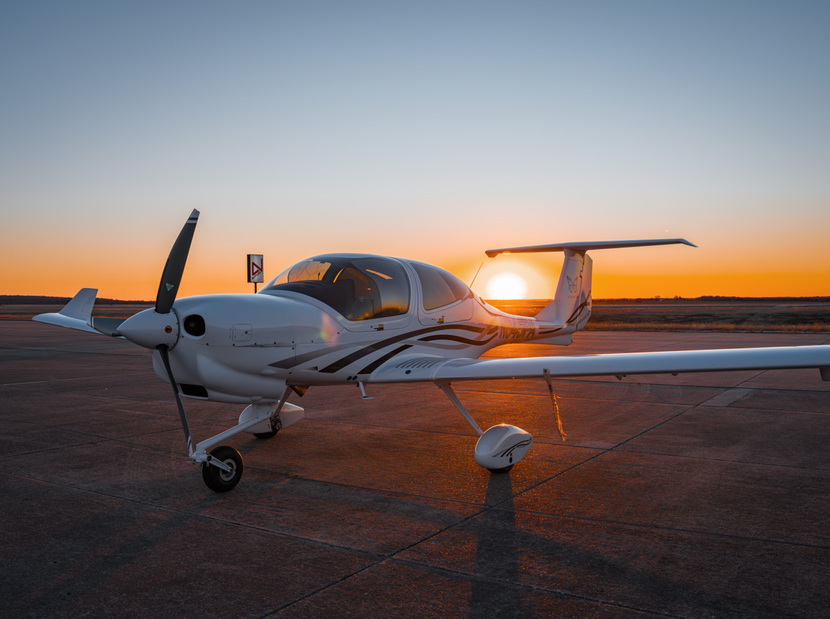 Small white airplane on tarmac with sunset in the background.