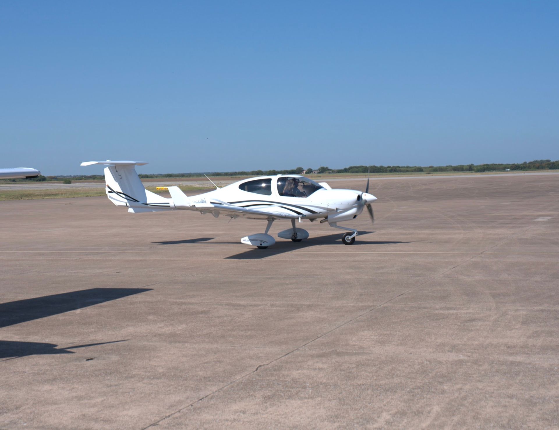 White airplane on a paved runway under a clear blue sky.