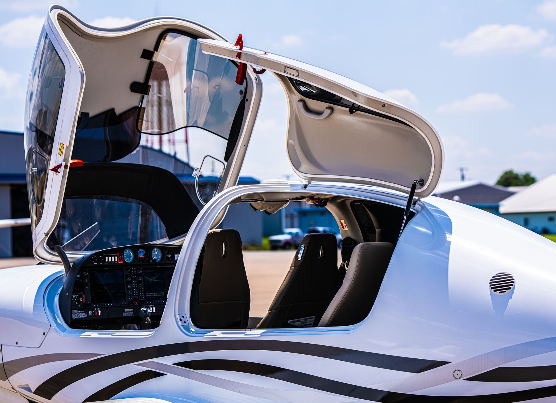 White airplane cockpit with open canopy, black seats, and control panel on tarmac.