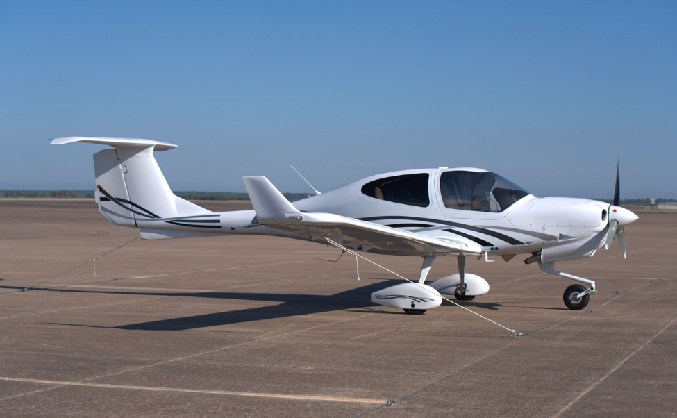White single-engine airplane parked on a paved surface on a sunny day.