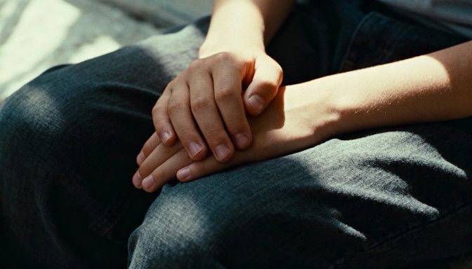 A close-up of younger hands folded and resting calmly on a lap, symbolizing inner peace after hypnosis.