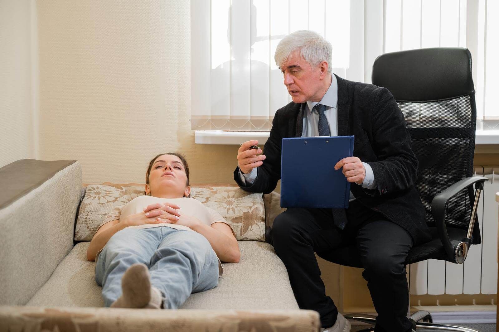 Photo of therapist sitting in his chair talking with a woman laying down on a couch