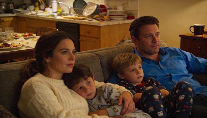 Fairborn husband and wife with young kids at home, lounging together on sofa after family dinner, cozy cluttered kitchen visible