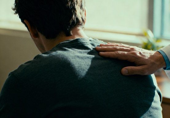 Therapist’s hand resting near client’s shoulder in a reassuring gesture, conveying empathy, professionalism, and trust.