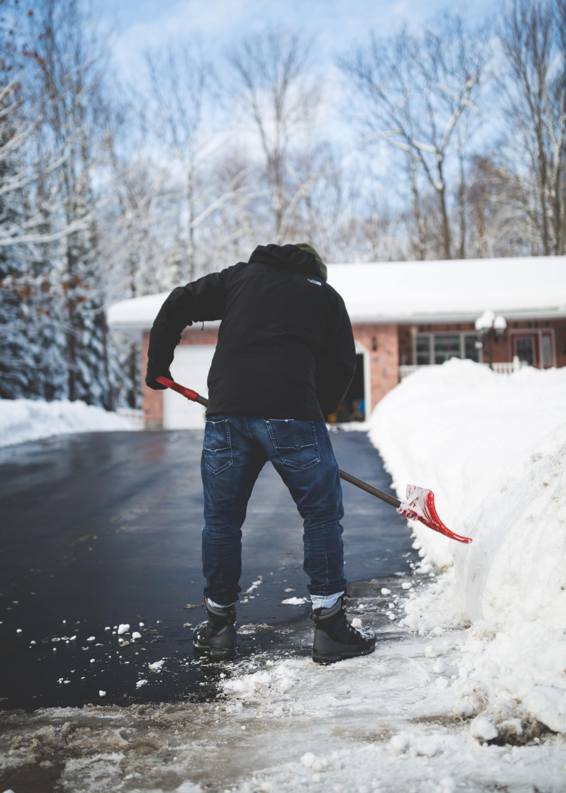 A man is shoveling snow from a driveway in front of a house.