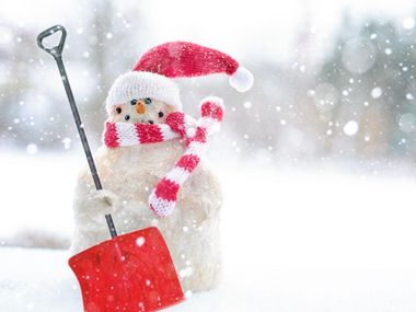 A snowman wearing a santa hat and scarf is holding a shovel in the snow.