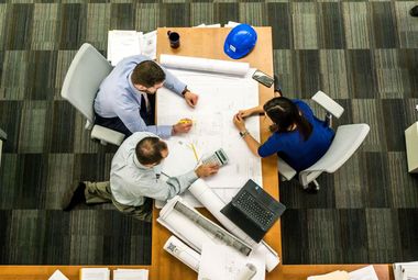 A group of people are sitting around a table looking at blueprints.