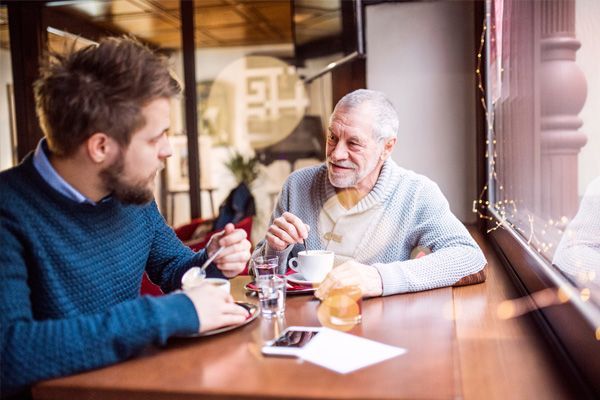 a man and an older man are sitting at a table in a restaurant talking .