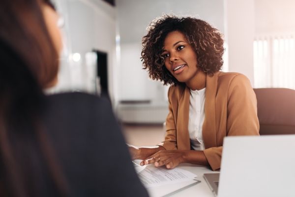 a woman is sitting at a desk talking to another woman .