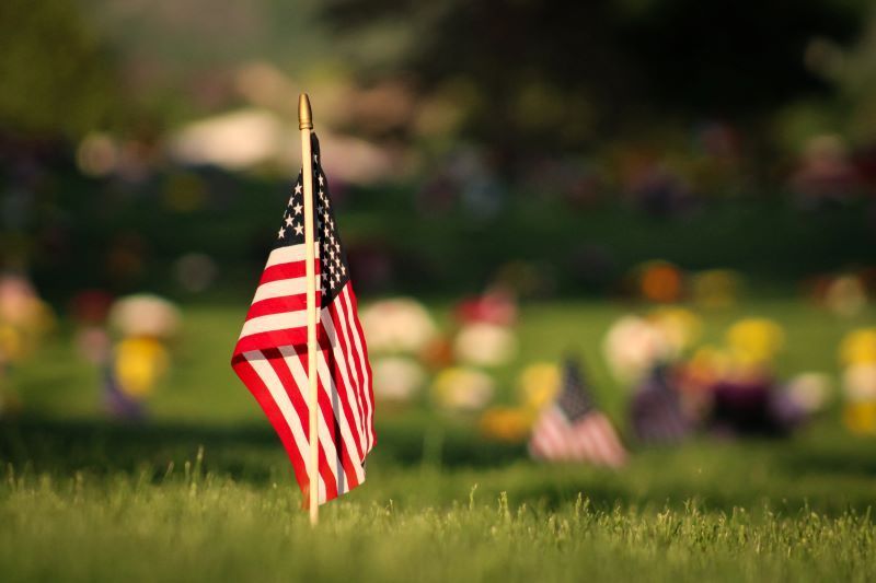 A small american flag is sitting in the grass in a cemetery.