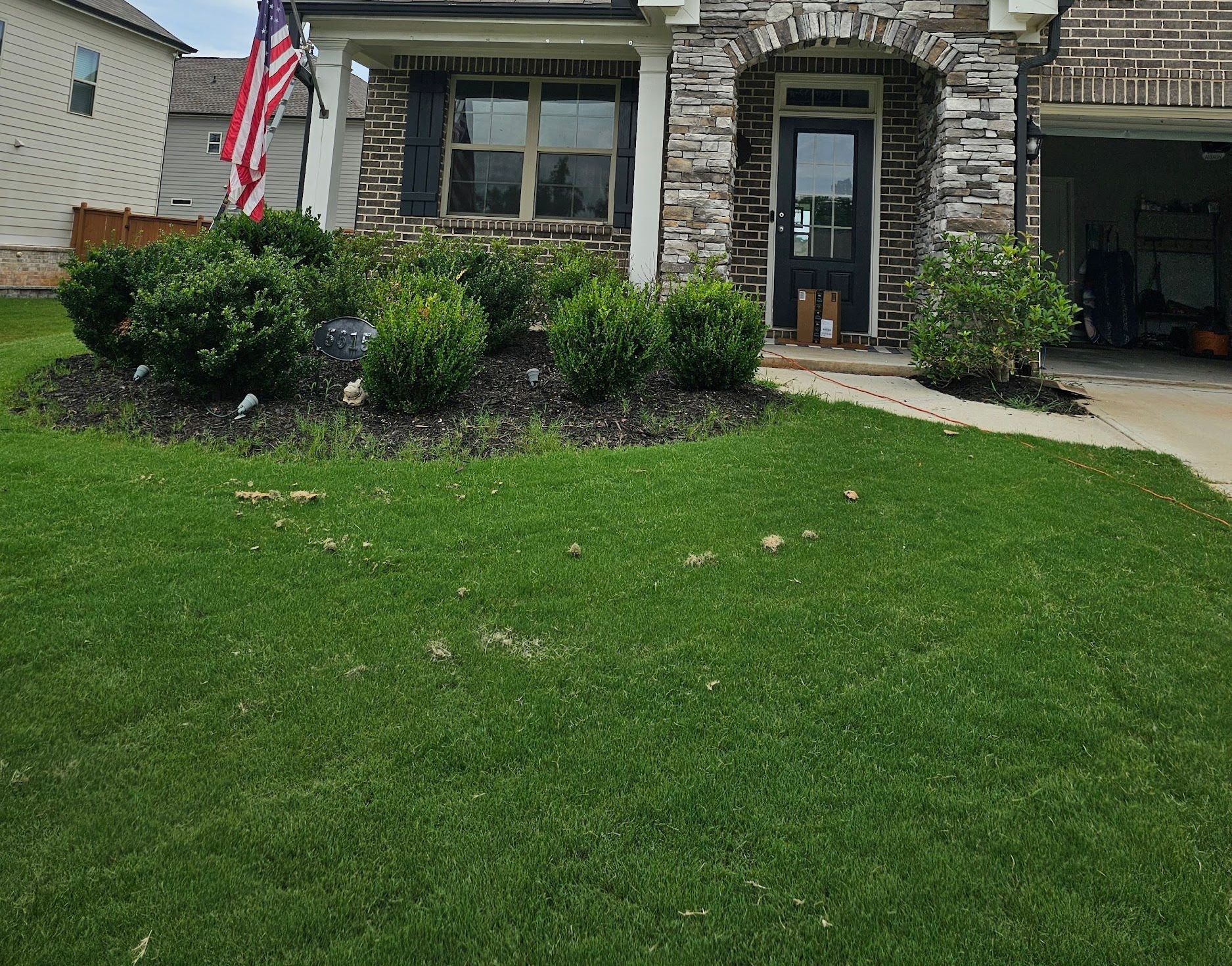 A house with a lush green lawn and an american flag in front of it.