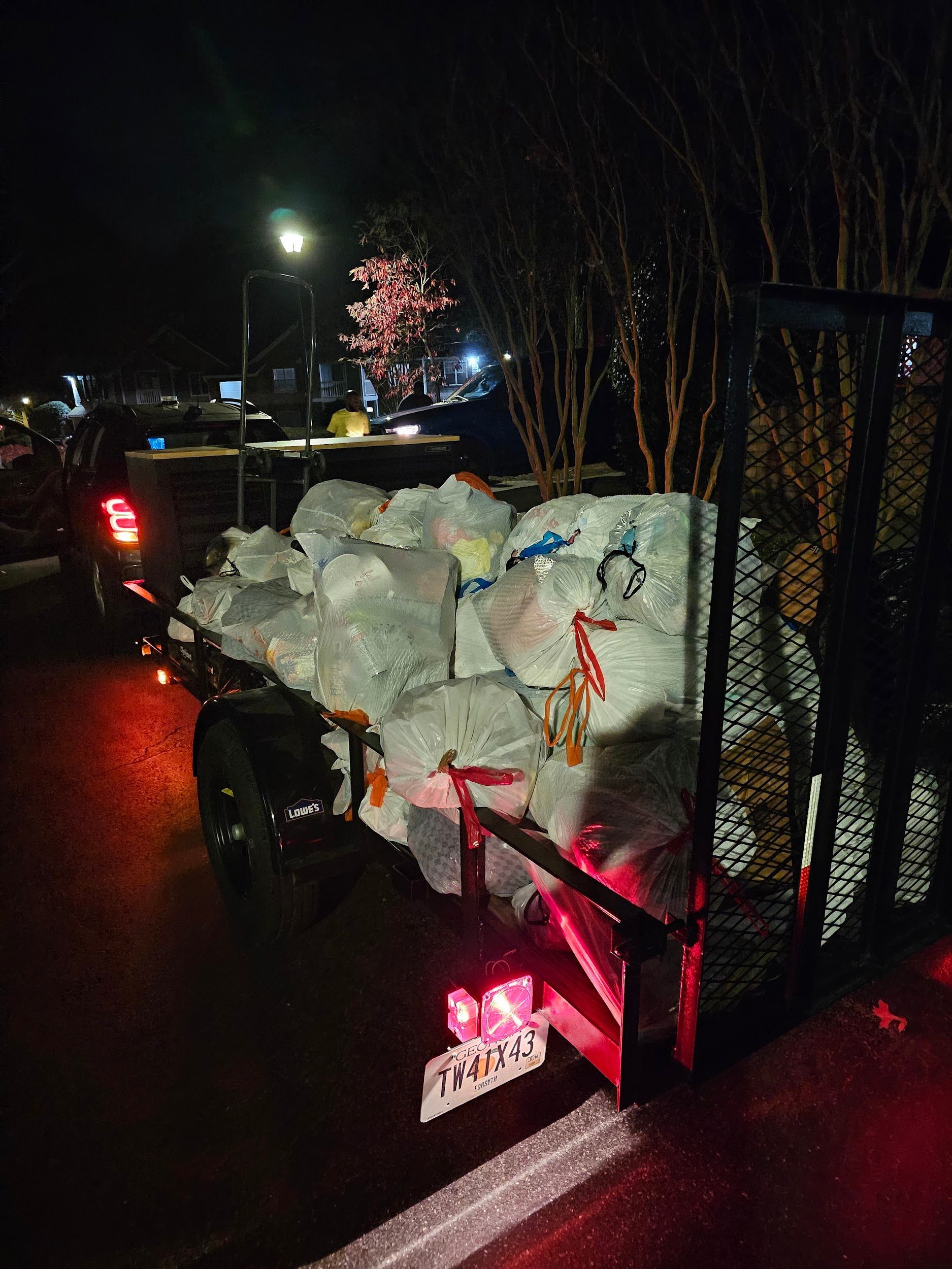 A truck with a trailer full of snow is parked on the side of the road at night.