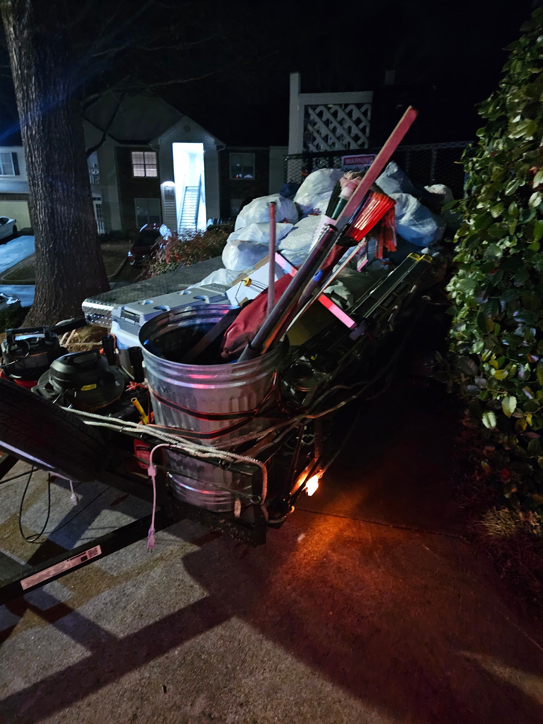 A wheelbarrow filled with trash is parked in front of a house at night.