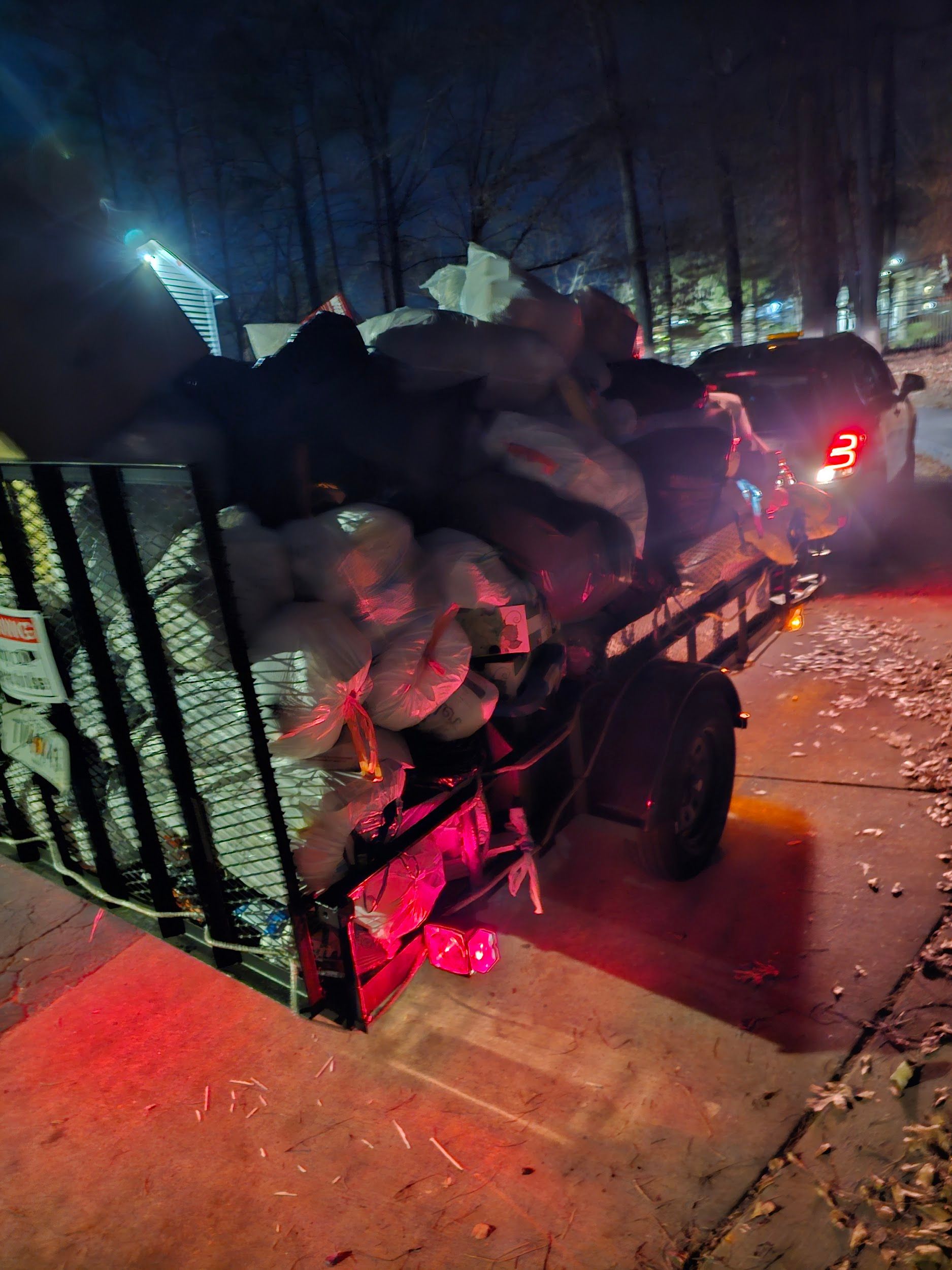 A truck with a trailer full of trash is parked on the side of the road at night.