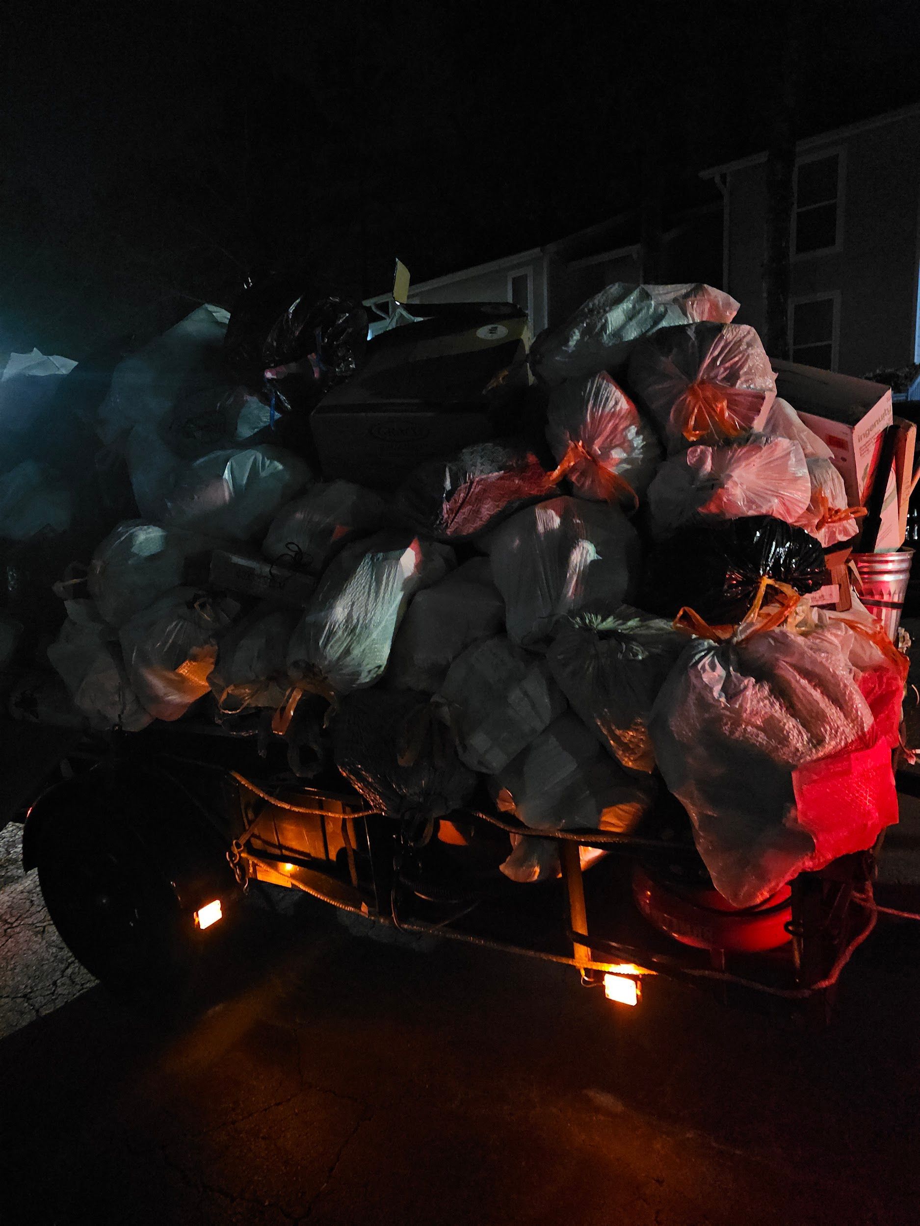 A large pile of garbage is on the back of a truck at night.