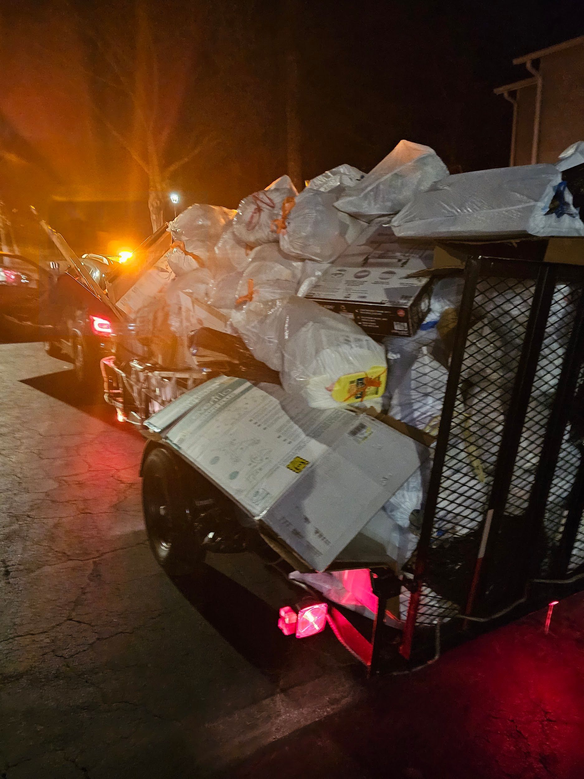 A trailer filled with lots of trash is parked on the side of the road at night.