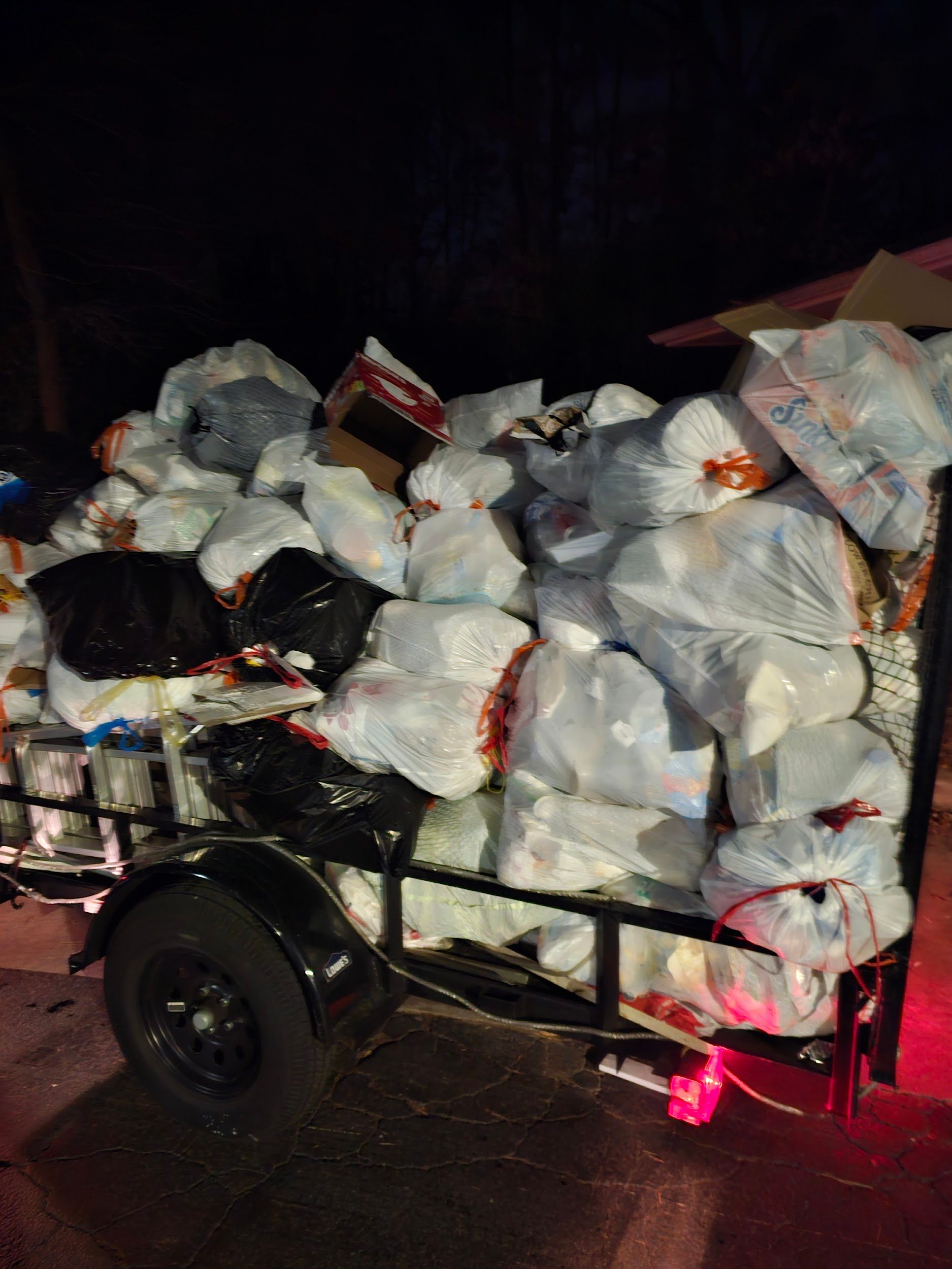 A trailer filled with lots of trash bags at night.