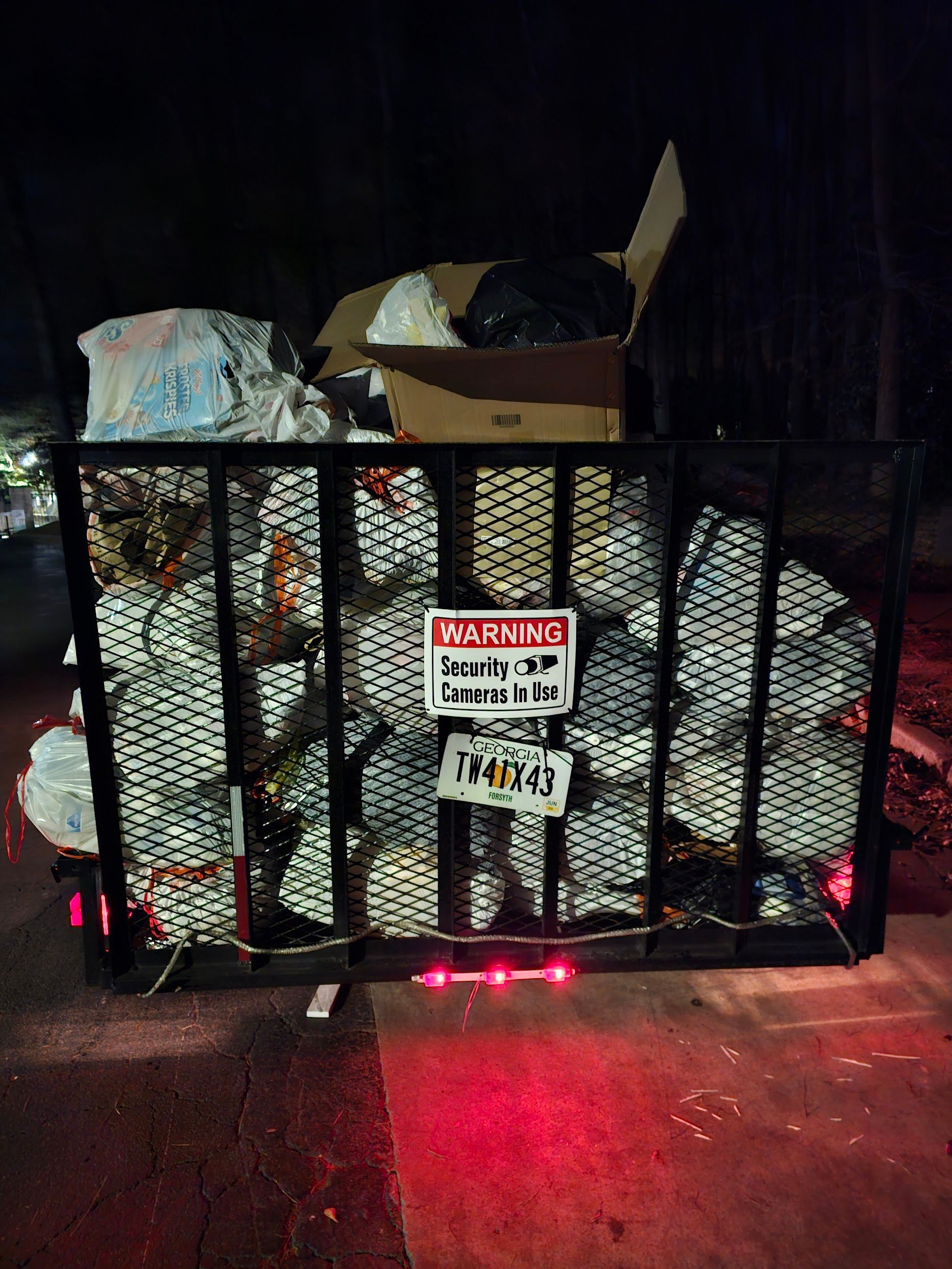 A pile of trash is behind a fence with a warning sign on it.