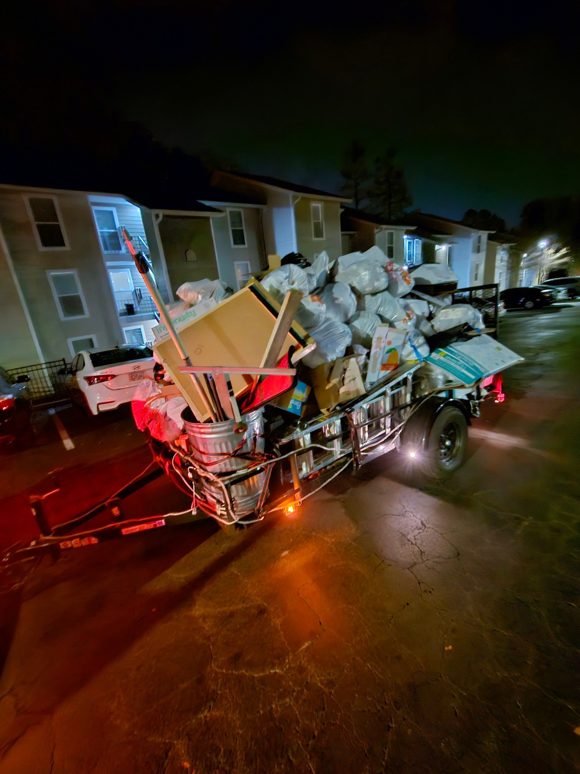 A trailer filled with junk is parked in front of a building at night.