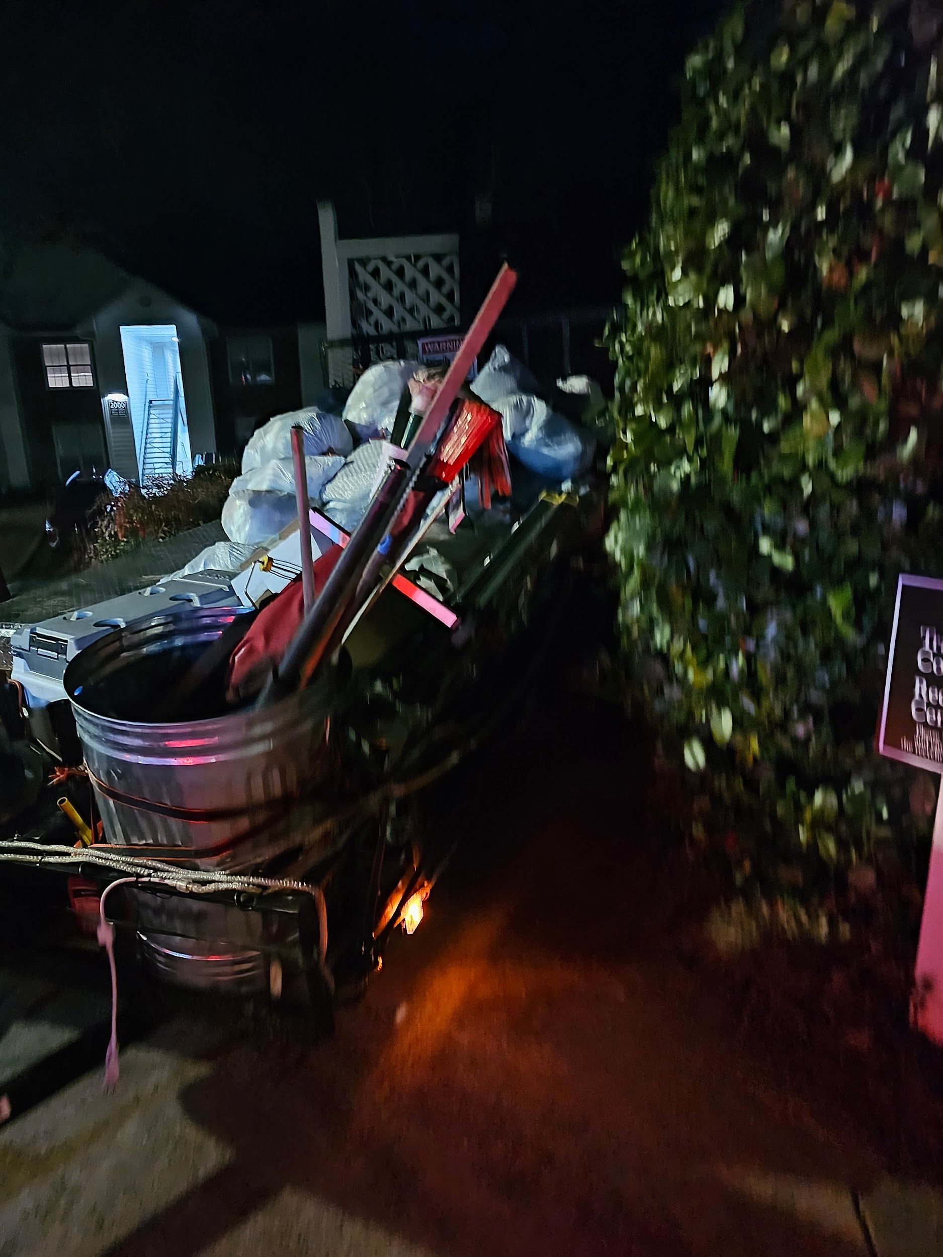 A trailer filled with lots of trash is parked in front of a house at night.