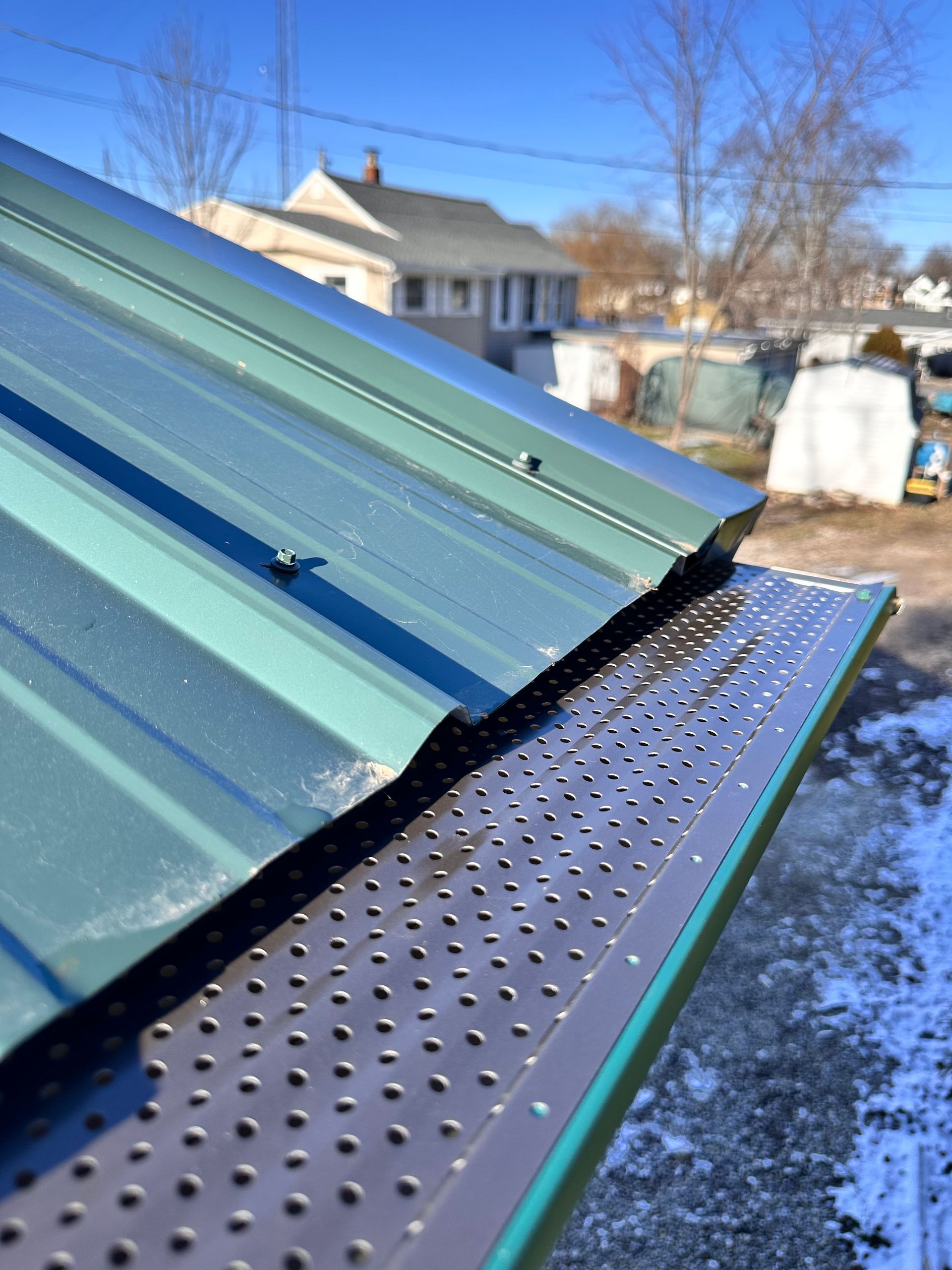 A green metal roof edge with a perforated brown gutter guard installed over the gutter.