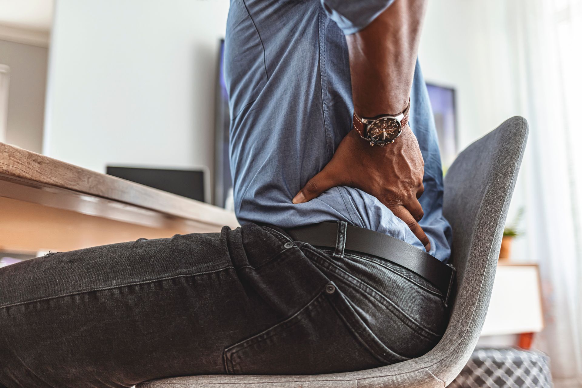 A man is sitting on a chair holding his back in pain.