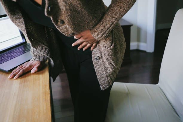 A woman is holding her stomach while standing in front of a laptop computer.