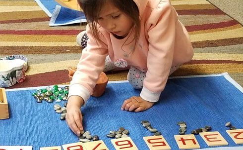 A little girl is playing with letters and coins on the floor.