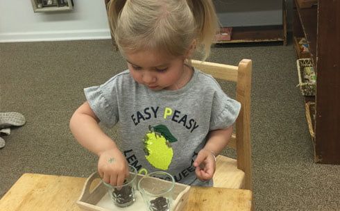 A little girl is sitting at a table playing with a tray.