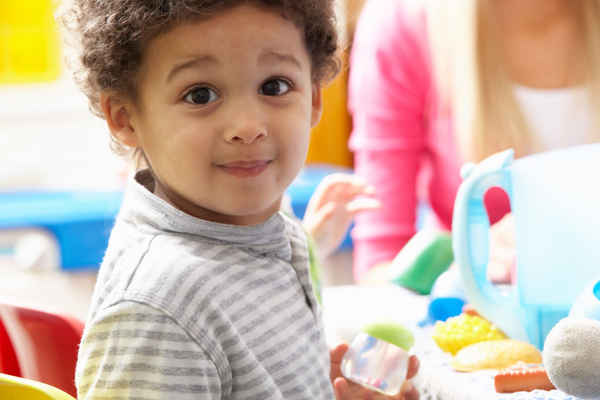 A young boy is sitting at a table with toys and looking at the camera.