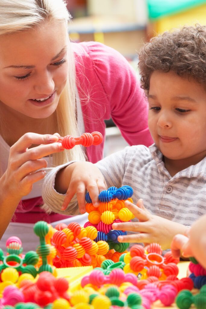 Young female preschool teacher helping facilitate montessori activities for 3 year olds