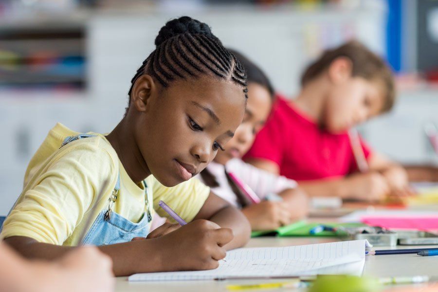 A group of children are sitting at desks in a classroom writing in notebooks.