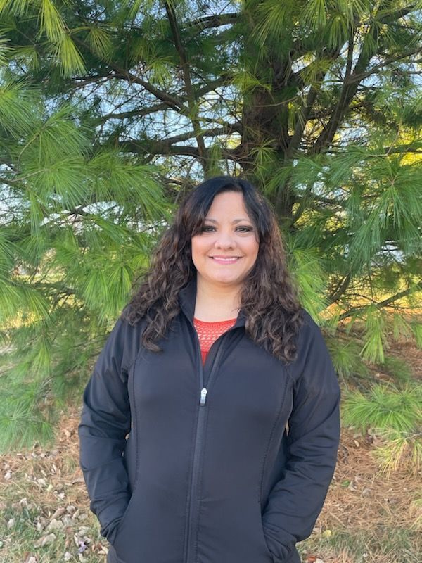 A woman is smiling in a circle with plants in the background.
