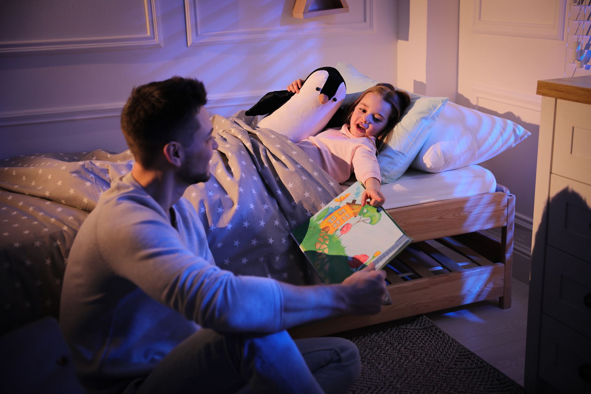 A man is reading a book to a little girl in bed.