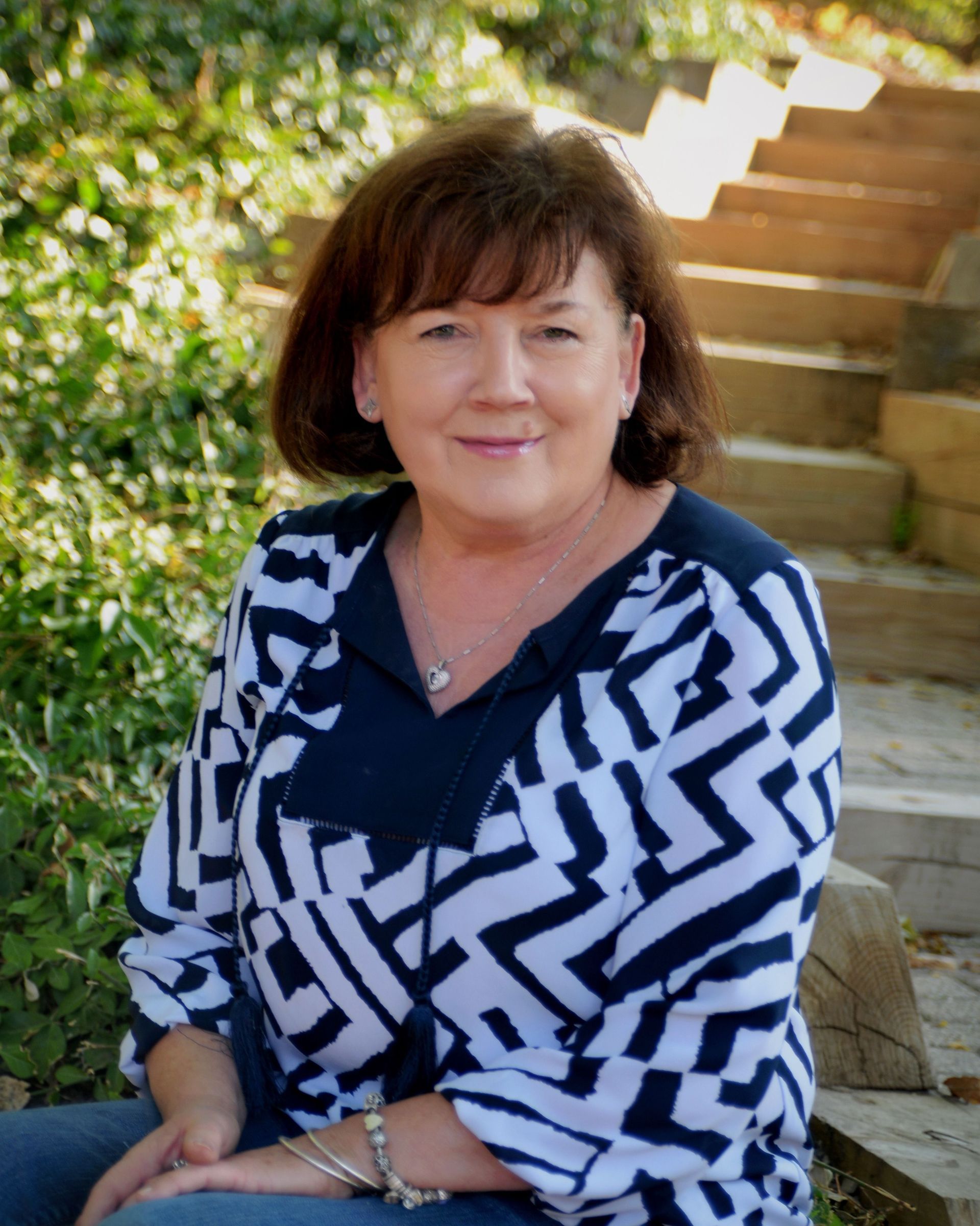 A woman wearing a black shirt and a necklace is smiling in a circle.