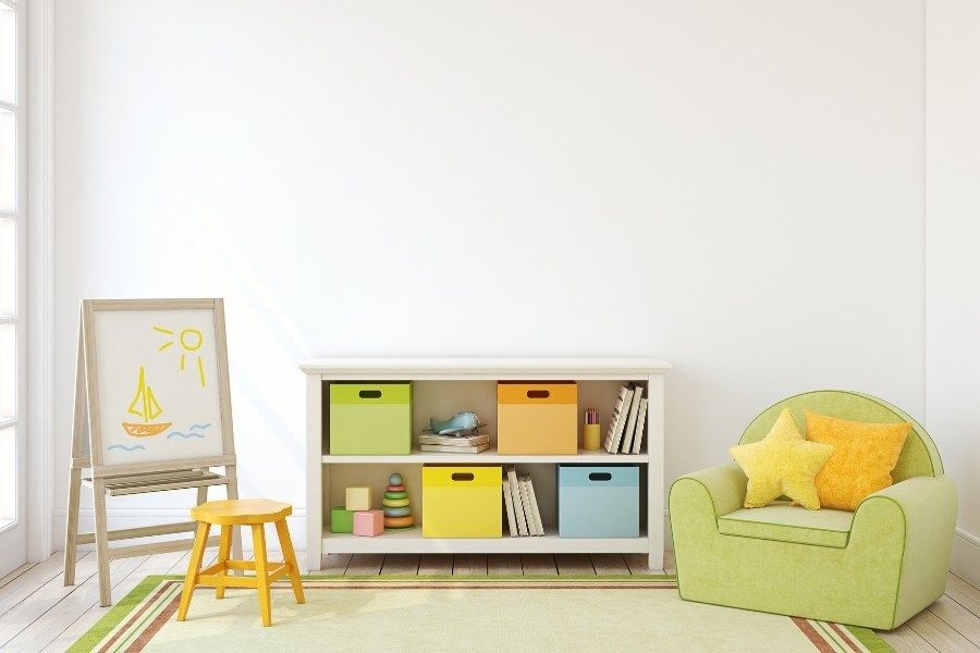 A child 's room with a green chair , a stool , a shelf , and a white board.