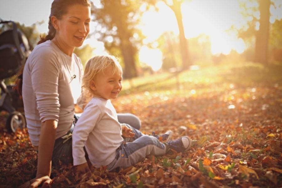 A woman and a child are sitting in the leaves in a park.