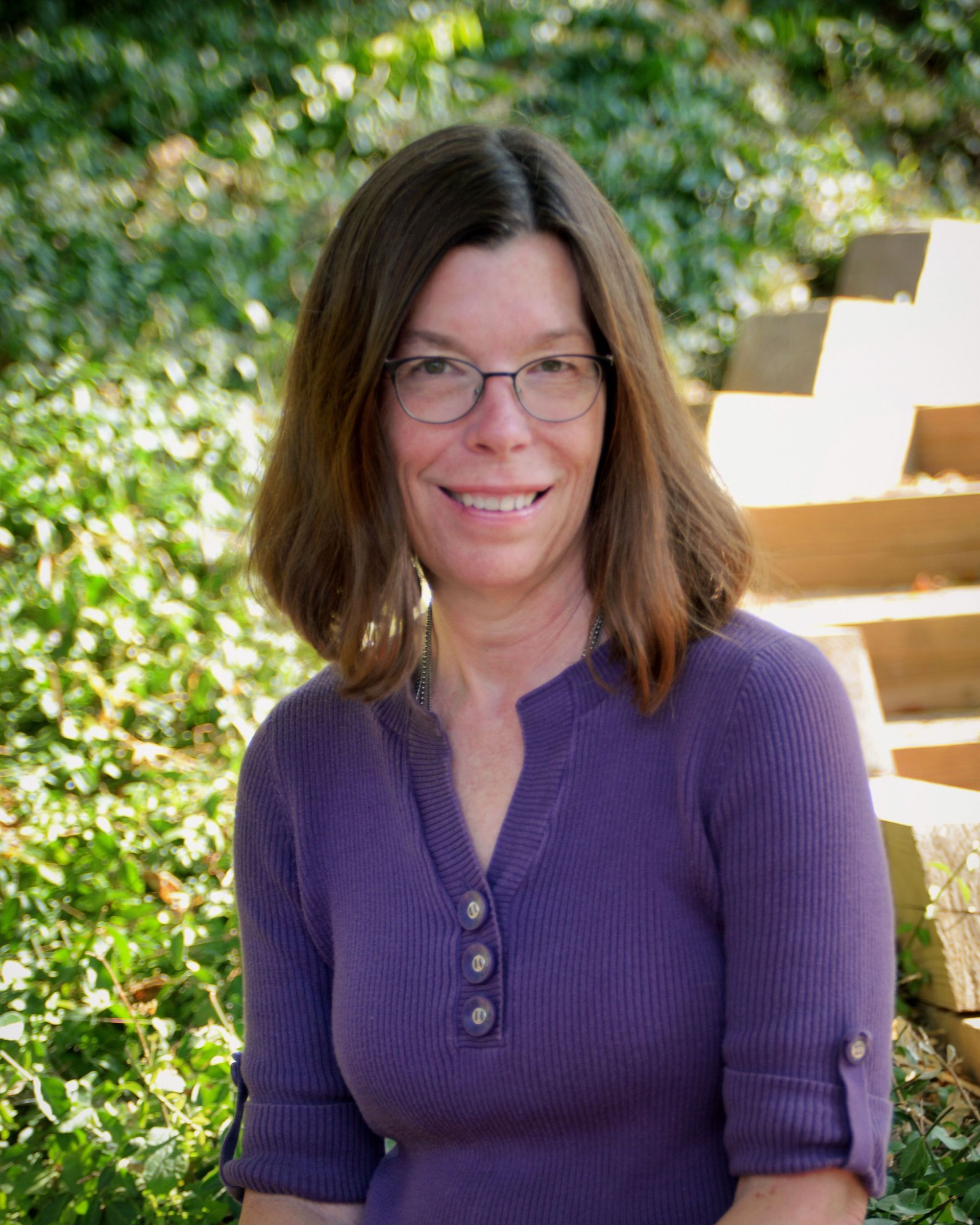 A woman is smiling in a circle with trees in the background