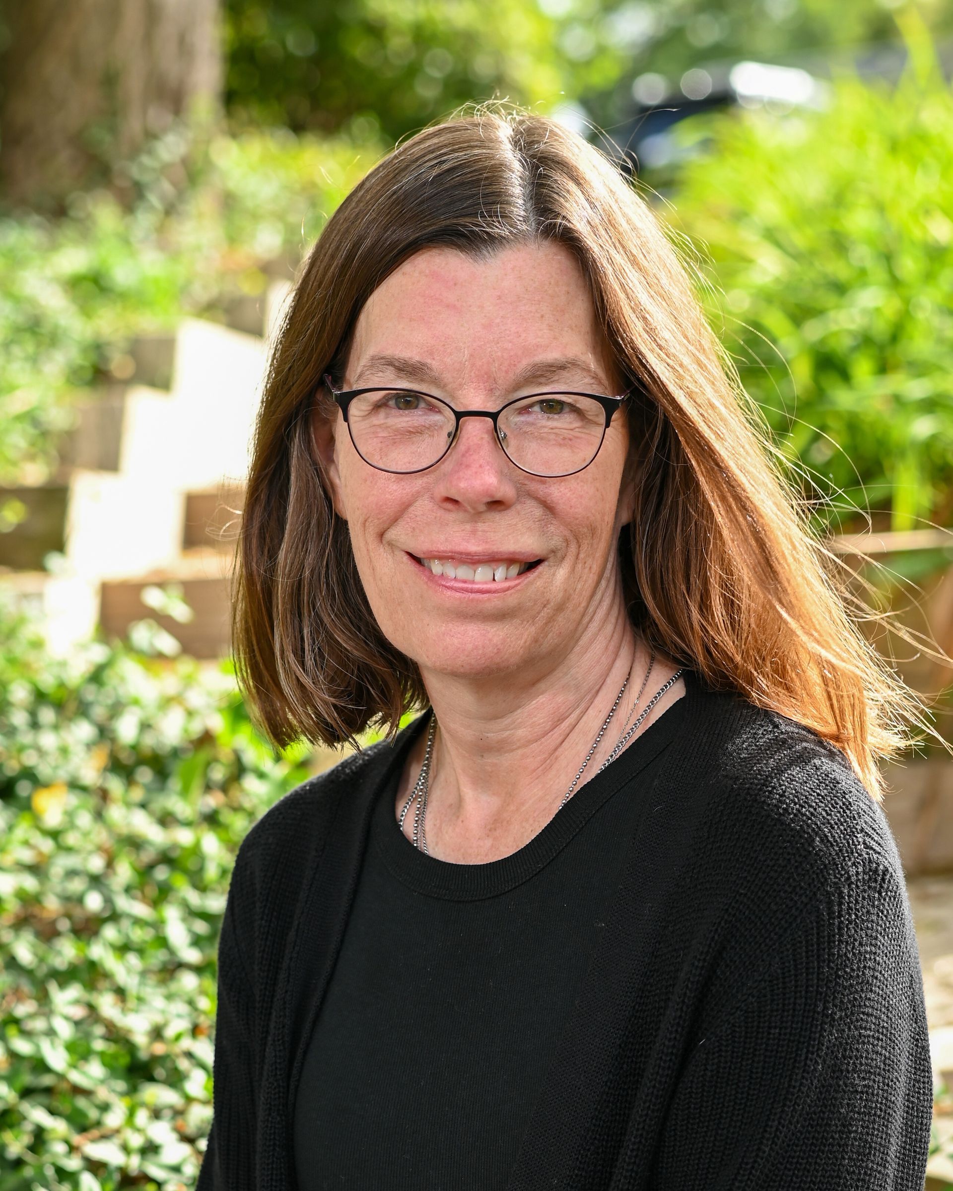 A woman is smiling in a circle with trees in the background