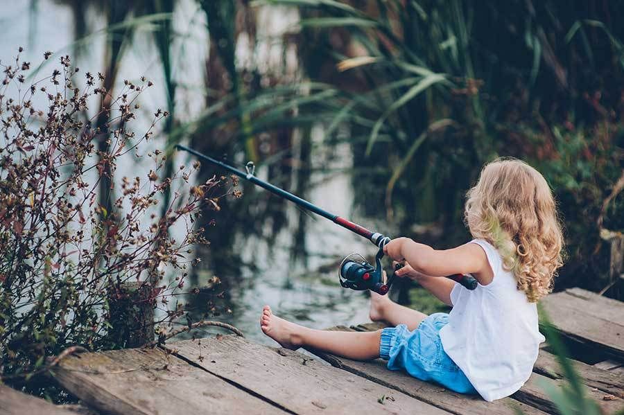 A little girl is sitting on a pier holding a fishing rod.