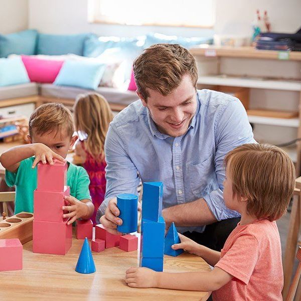 A man is playing with blocks with two children at a table.