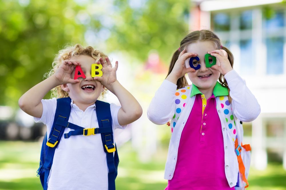 A boy and a girl are holding alphabet letters in front of their eyes.