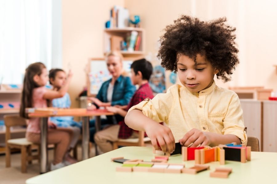 A young boy is playing with wooden blocks at a table in a classroom.