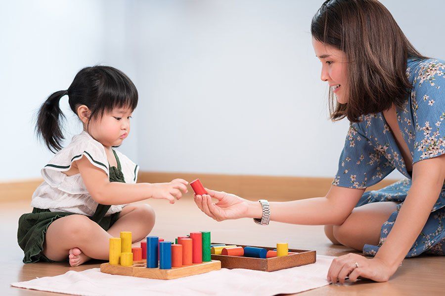 A woman and a little girl are playing with wooden blocks on the floor.