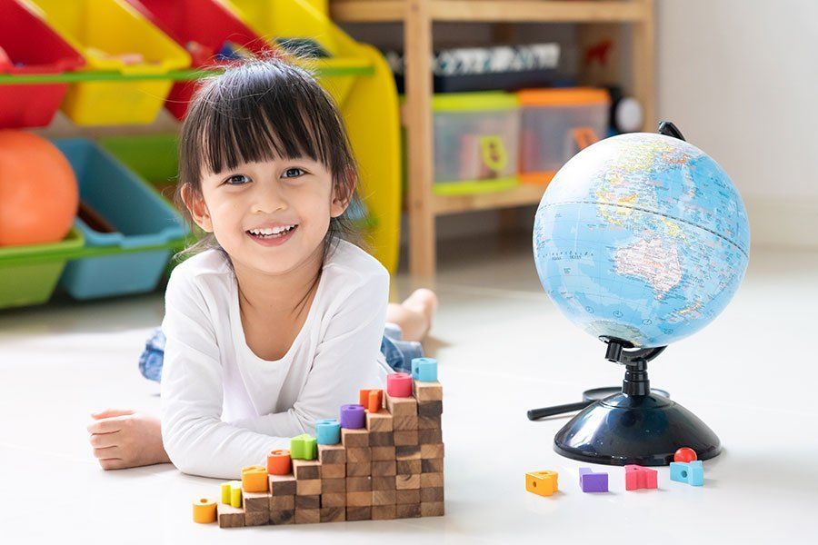 A little girl is laying on the floor next to a globe and wooden blocks.