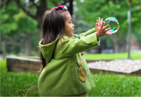 A little girl is playing with soap bubbles in a park.