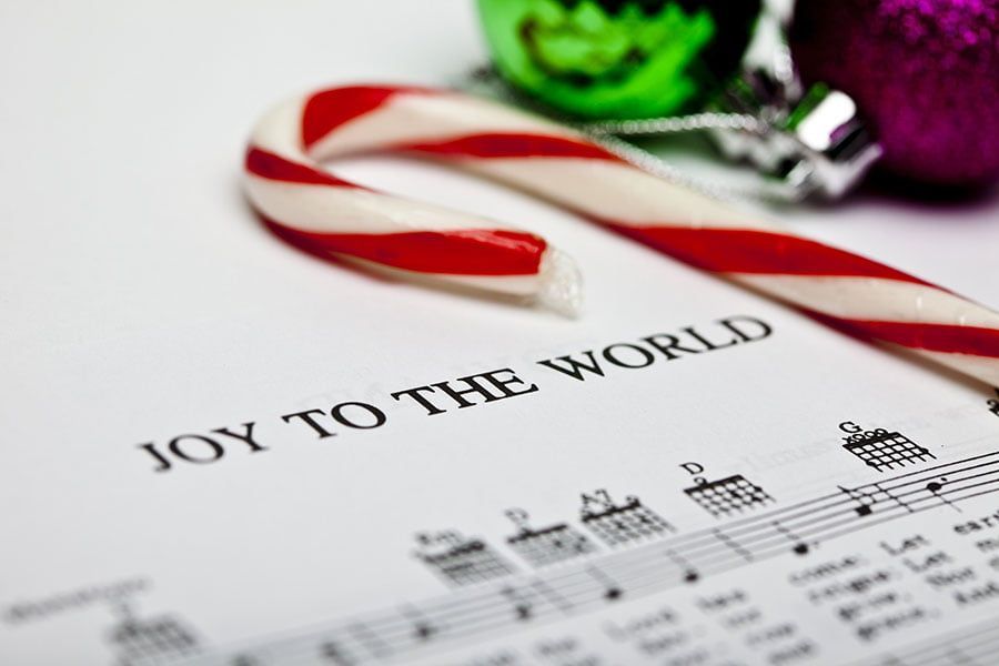 A candy cane sits on top of a sheet of music that says joy to the world